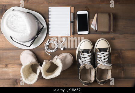 Travel preparations on wooden table, hat wallet, bag, notebook, kid boot, mobile phone and sneakers. Stock Photo