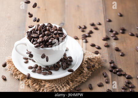 motion fresh coffee bean falling to white cup on wood background Stock Photo