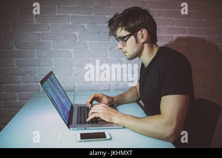 Young man programer work on laptop in the night and hack the network. Young hacker attack a network in the night. Hacker Stock Photo