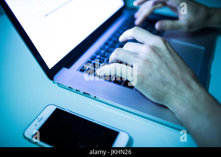 Close up of male hands typing on keyboard with white screen in the night. Hacker Stock Photo