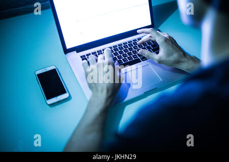Close up of male hands typing on keyboard with white screen in the night. Hacker Stock Photo