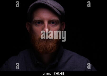 Young Redhead Male looking into camera in a dark background Stock Photo