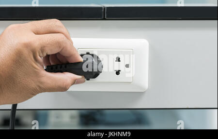 hand unplugging a plug from a socket, metaphor for saving electrical energy Stock Photo
