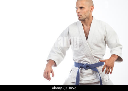 A young bald man in a white kimono and blue belt for a kimono, sambo, jiujitsu stands in a fighting pose on an isolated white background Stock Photo