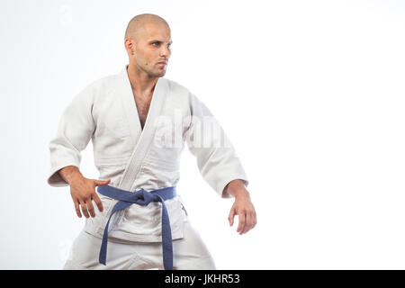 A young bald man in a white kimono and blue belt for a kimono, sambo, jiujitsu stands in a fighting pose on an isolated white background Stock Photo