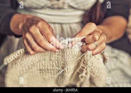 Close-up of an adult woman with dark hair braided in a braid, in a striped sweater knits a white sweater Stock Photo