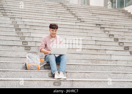 Handsome student in shirt working on laptop sitting on stairs in college Stock Photo