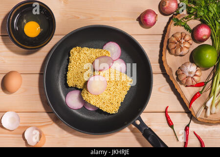 Instant noodles for cooking and eat in the dish with eggs and vegetables on wooden background. Stock Photo