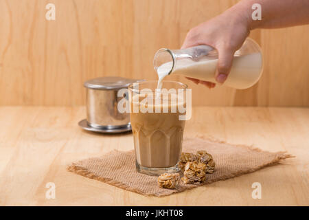 Pouring milk in to glass of coffee on a wooden table. Stock Photo