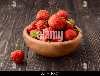 Ripe strawberries in wooden bowl and green leaves on old table, top view Stock Photo