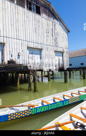 Dragon boats tied up by an old net loft building at Steveston in British Columbia Stock Photo