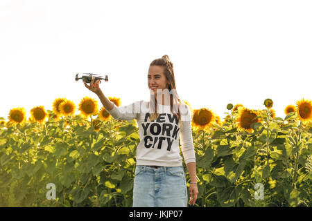 Beautiful woman is holding a mini dron on the background of a field sunflowers. Stock Photo