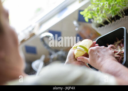 Senior woman peeling red potatoes, preparing food. Horizontal orientation with selective focus on potatoe and peeler. Natural day light Stock Photo