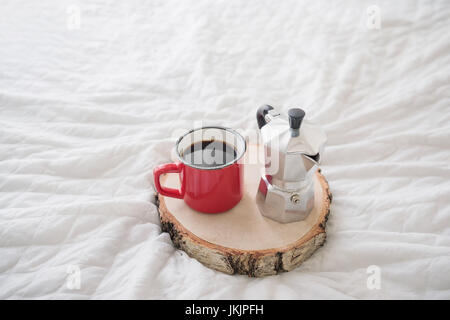 Red mug of coffee with coffee maker on wooden tray on white bed Stock Photo