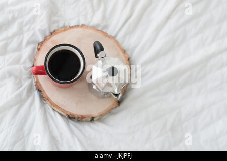 Top view of red mug of coffee with coffee maker on wooden tray on bed Stock Photo