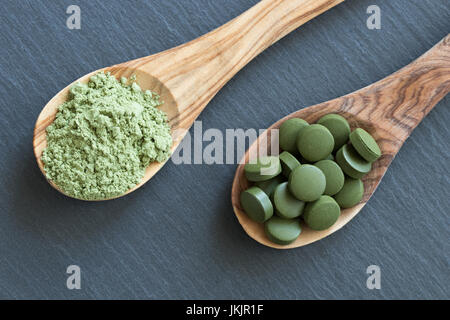 Chlorella tablets and young green barley powder on two wooden spoons on a dark background Stock Photo