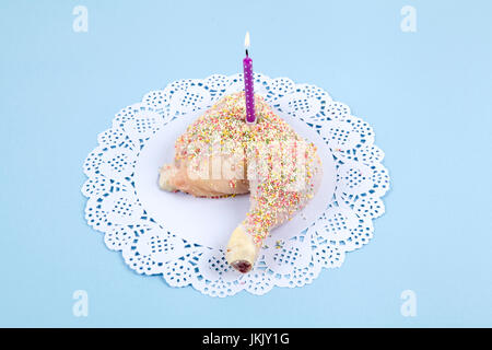 a quirky birthday chicken thigh covered with sprinkles like cake on blue pastel background. Minimal and funny design still life photography. Stock Photo
