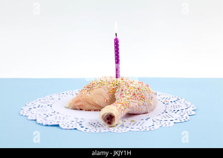 a quirky birthday chicken thigh covered with sprinkles like cake on blue pastel background. Minimal and funny design still life photography. Stock Photo