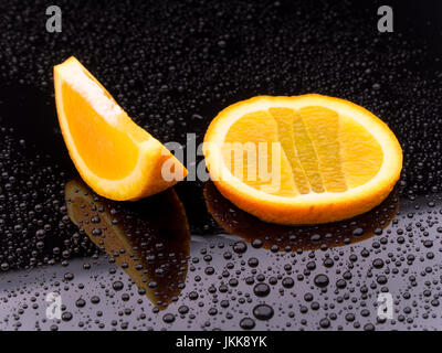 Healthy orange fruit slices on a black surface with reflection and water droplets Stock Photo