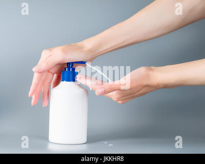 Woman hands pouring liquid soap from dispenser. On gray background Stock Photo