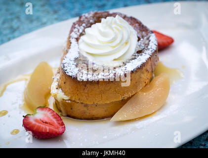Beautifully plated cinnamon French toast (eggy bread) with whipped cream, maple syrup, vanilla poached pears, and strawberries. Stock Photo