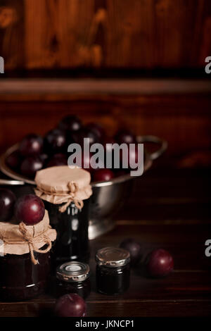 Ripe plums and jars with plum jam on a wooden background. Selective focus. Stock Photo