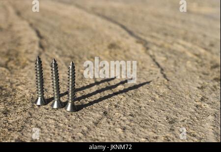 Three metal screws standing on end close up against plain background, casting long shadows. Stock Photo