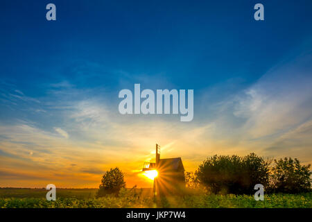 Summer. An old wooden windmill surrounded by sunflowers. The sun rises behind the windmill and paint the sky in beautiful colors Stock Photo