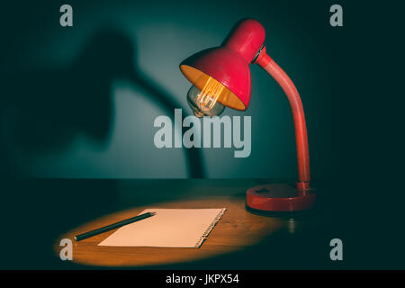 Table lam with old fashioned bulb lighting onto blank piece of paper with pencil on it Stock Photo