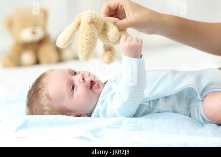 Mother hand holding a teddy and playing with her baby son on a bed Stock Photo