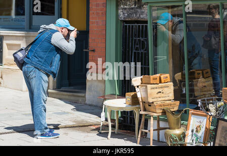Photographer taking a photo through a shop window with his reflection in the window. Stock Photo