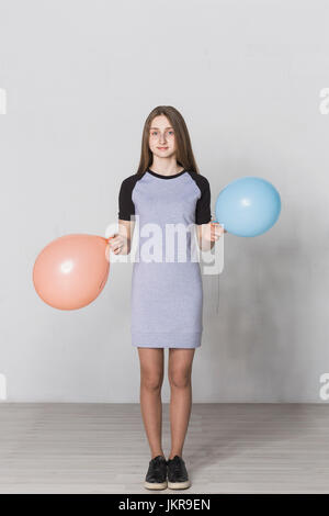 Portrait of teenage girl holding balloons standing against white wall Stock Photo