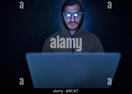 Serious computer hacker wearing hooded shirt using laptop against black background Stock Photo
