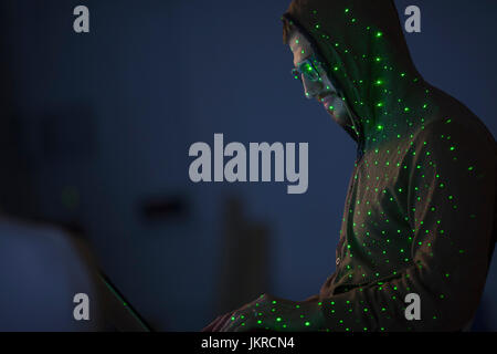 Green lights over computer hacker wearing hooded shirt using laptop Stock Photo