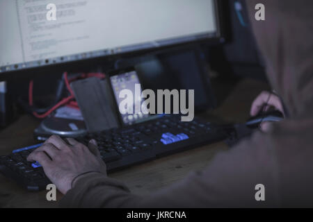 Cropped image of computer hacker with smart phone at table Stock Photo