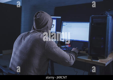 Computer hacker wearing hooded shirt using computer at table Stock Photo
