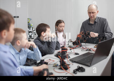 Students looking at teacher operating machinery at table in classroom Stock Photo