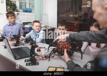 Teacher showing machinery to students sat table in classroom Stock Photo