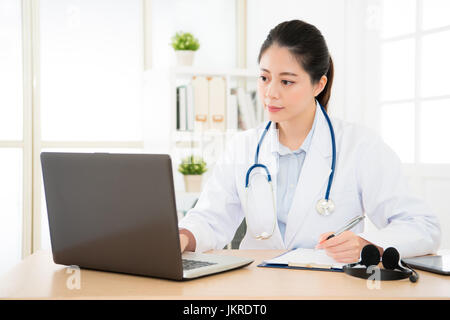 professional doctor seriously searching medical records about new patient through online medicine system and writing note on the paper board research  Stock Photo