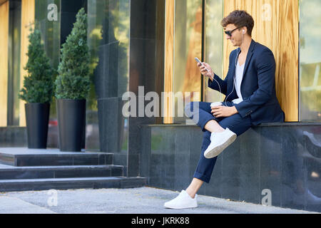 Side view portrait of stylish contemporary man relaxing outdoors enjoying music from  smartphone and smiling happily Stock Photo