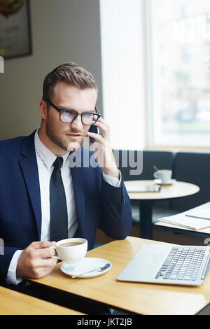 Businessman talking on smartphone by cup of tea Stock Photo