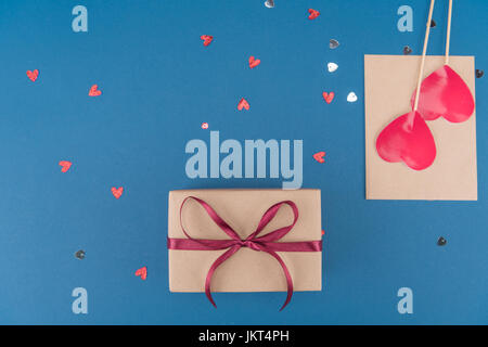 top view of gift box, heart shaped confetti and envelope isolated on blue, birthday party concept Stock Photo