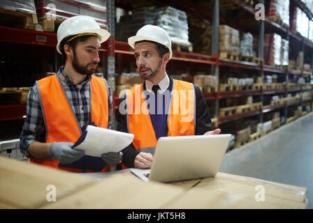 Portrait of two warehouse workers doing inventory of stock, manager talking to loader while using laptop to enter data from goods lists  Stocktaking i Stock Photo