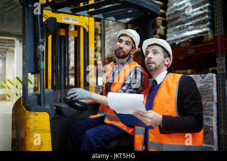 Portrait of warehouse manager and loader riding forklift truck inventorying stock Stock Photo
