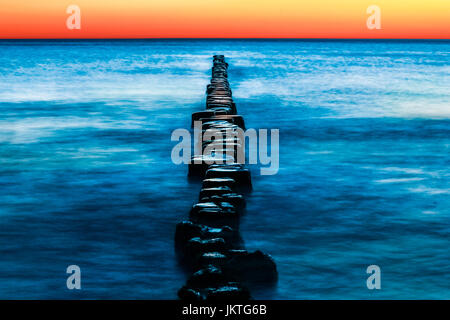 Wooden groynes with blue water and red sunset. Long exposure. Stock Photo