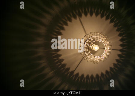 Chandelier with illuminated lightbulb casts patterned shadow onto ceiling. Space for text. Stock Photo