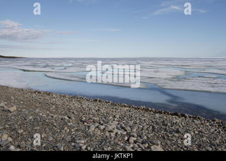 Broken pans of sea ice on ocean coast with blue sky and pebble beach along the Northwest Passage in June, Cambridge Bay, Nunavut Stock Photo