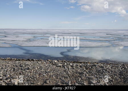 Broken pans of sea ice on ocean coast with blue sky and pebble beach along the Northwest Passage in June, Cambridge Bay, Nunavut Stock Photo