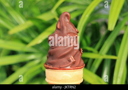 Chocolate Dipped Soft Serve Ice Cream Cone, with Blurred Green Foliage in Background Stock Photo