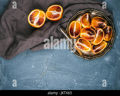 Bloody red sicilian oranges cut into quarters in vintage metal plate over concrete textured background Stock Photo